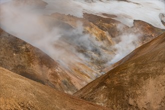 Steaming stream between colourful rhyolite mountains and snowfields, Hveradalir geothermal area,