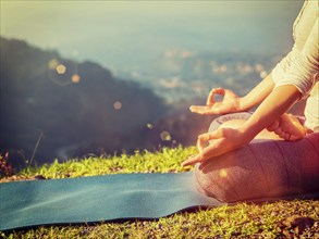 Close up of woman in Padmasana yoga lotus pose with chin mudra outdoors with copyspace. With light