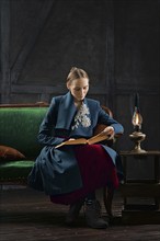 Attractive lady in oldfashioned clothes reading ancient book near vintage kerosene lamp