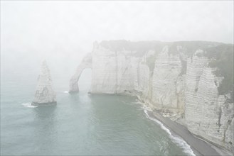 L'Aiguille and the Porte D'Aval, a natural arch in the chalk cliffs at Etretat in the mist, Côte