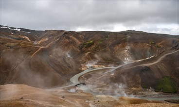 Bridge and steaming streams between colourful rhyolite mountains in the Hveradalir geothermal area,