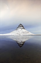 Kirkjufell, nunatak hill covered in snow reflected in water of fjord on the Snæfellsnes peninsula