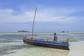 Malagasy fisherman dragging traditional wooden fishing boat, outrigger canoe to sea at Andavadoaka