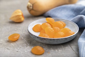 Jelly pumpkin candies on gray concrete background and blue linen textile. close up, side view,