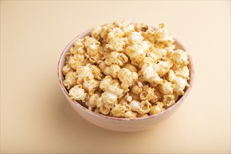 Popcorn with caramel in ceramic bowl on pastel orange background. Side view, close up