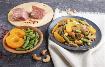 Fried pork with peaches, cashew and green beans on a black concrete background. side view, close