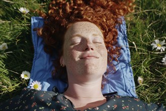 Teenager, young fair-skinned woman with red hair and freckles lying on a spring meadow and basking