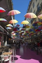 Street with colourful umbrellas over café tables and people under a clear blue sky, Pink Street,