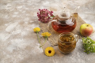 Red tea with herbs in glass teapot on brown concrete background and linen textile. Healthy drink