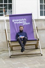 Young man sitting in giant deckchair outside the Students' Union, Greenwich, London SE10, England,