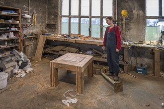 Young man standing in front of his finished table in the Wertkstatt, Mecklenburg-Vorpommern,