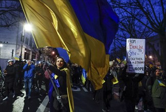 A woman with a large Ukrainian flag demonstrates in front of the Russian embassy on the anniversary