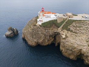 A red lighthouse and white buildings on a rocky cliff overlooking the ocean, an isolated feeling,