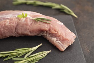 Raw pork meat with herbs and spices on slate cutting board on black concrete background. Side view,