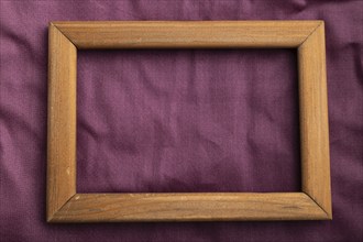 Wooden frame on smooth cotton purple tissue. Top view, flat lay, natural textile background and