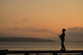 Boy at sunset standing on a pier and fishing for salmon, Vancouver Island