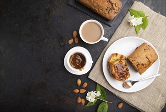 Homemade cake with raisins, almonds, soft caramel and a cup of coffee on a black concrete