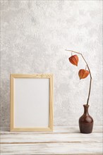 White wooden frame mockup with physalis in ceramic vase on gray concrete background. Blank,