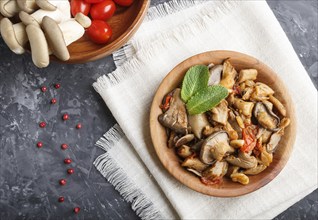 Fried oyster mushrooms with tomatoes in wooden plate on black concrete background. top view, close