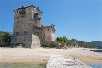 Ancient stone watchtower on the beach under a clear blue sky, surrounded by green vegetation and