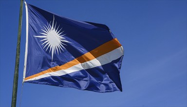 The flag of the Marshall Islands, Pacific Islands, flutters in the wind, isolated against a blue