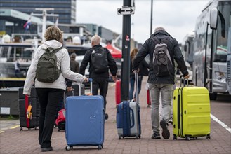 Travellers on their way to a river cruise ship at the quay of the Ij, transporting their luggage,