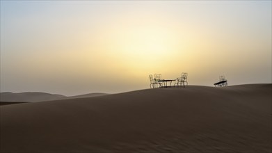 Sunset, cast iron table and chairs in the sand dunes of Erg Chebbi, Sahara, Merzouga, Morocco,