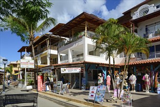 A lively street scene in a tropical town with wooden architecture and various shops, Bayahibe,