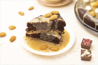 Pieces of chocolate brownie cake with caramel cream and almonds on a white concrete background.