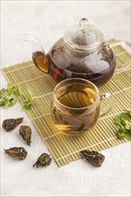 Red tea with herbs in glass on gray concrete background and linen textile. Healthy drink concept.