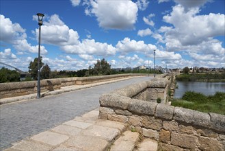 View of an old stone bridge with cobblestones against a clear blue sky and white clouds, Roman