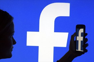 Silhouette of a woman with a smartphone in her hand in front of a Facebook logo, 12/01/2016