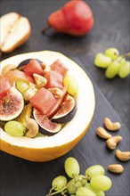 Vegetarian fruit salad of watermelon, grapes, figs, pear, orange, cashew on slate board on a black