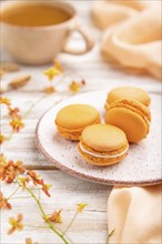 Orange macarons or macaroons cakes with cup of apricot juice on a white wooden background and