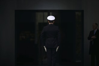 A marine stands with his back to the camera in front of the entrance to the Federal Chancellery.