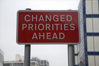 Road sign saying Changed Priorities Ahead on red background, UK