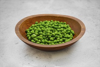 Thawed fresh green peas in a wooden bowl on a grey stone table