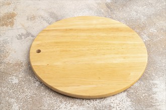 Empty round wooden cutting board on brown concrete background. Side view, close up