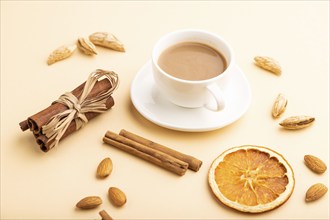 Composition with almonds, cinnamon and cup of coffee on orange pastel background. Blank, side view,