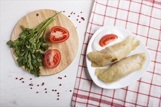 Cabbage rolls with beef, rice and vegetables on a linen tablecloth on a white wooden background.