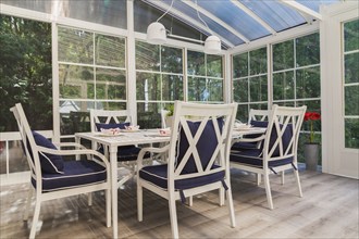 White dining table and armchairs with blue cushions in sunroom at back of luxurious residential