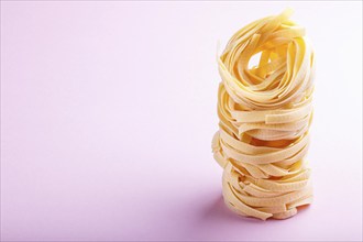 Raw uncooked tagliatelle pasta on a pink pastel background. side view, close up, copy space