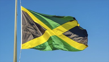 The flag of Jamaica flutters in the wind, isolated against a blue sky