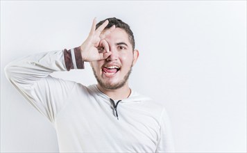 Funny young man making OK gesture looking through fingers isolated. Happy guy making ok gesture