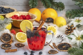 Punch in a glass cup, surrounded by oranges, lemons, raspberries and Christmas decorations