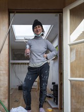 Young woman painting Luton van interior as part of a conversion project, UK