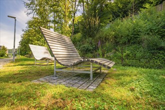 Several wooden loungers in a sunny park surrounded by green vegetation, Nagold, Black Forest,