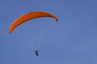 An orange paraglider in the blue sky