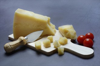 A piece of Parmesan cheese and chopped pieces of cheese on a wooden board