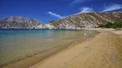 Long, unspoilt beach with turquoise water and mountains in the background, lined with trees, Psili